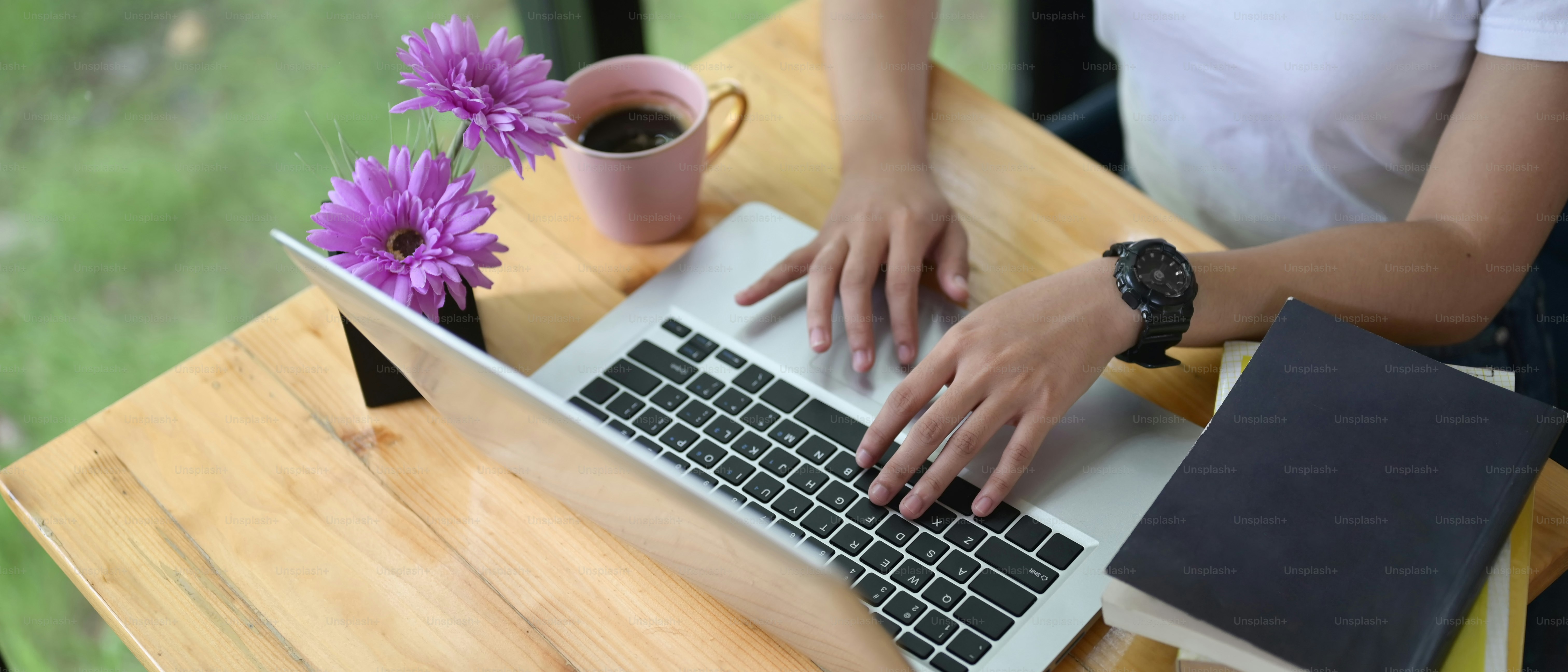Cropped image of the hand is typing a computer laptop at the wooden working desk.