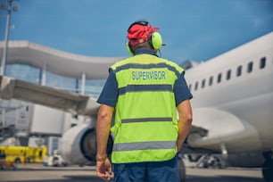 Back view of a supervisor in noise-canceling headset standing in front of a large airliner