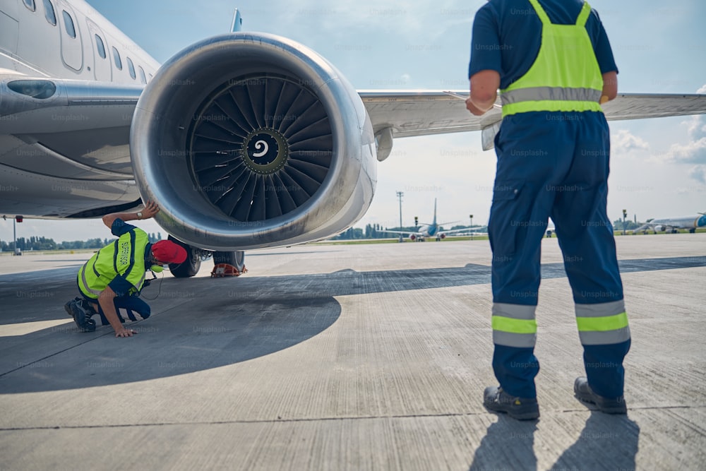 Back view of two professional aircraft maintenance mechanics inspecting an airplane motor before the takeoff