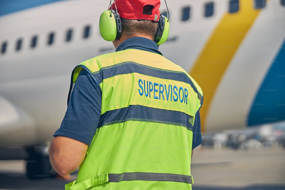 Back view of an aircraft maintenance supervisor in headphones standing in front of an airplane