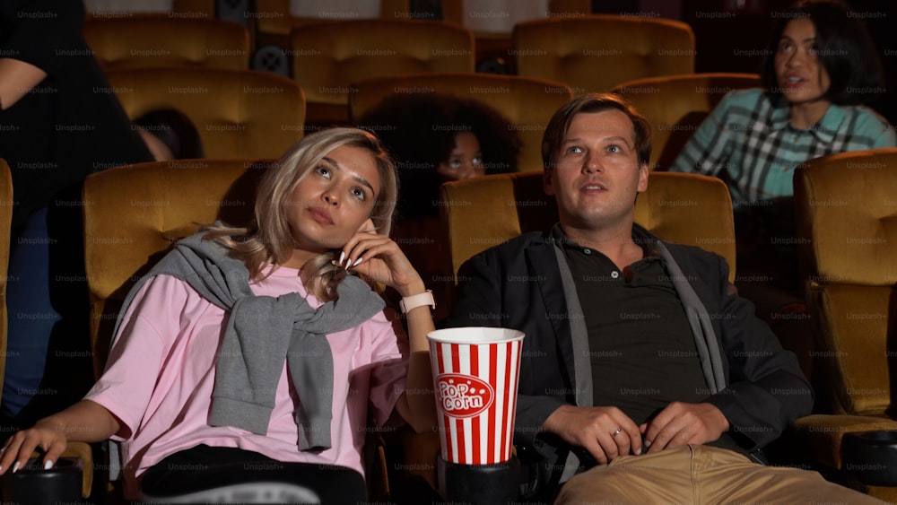 Público caminhando para os assentos no cinema, assistindo a filmes e comendo pipoca.