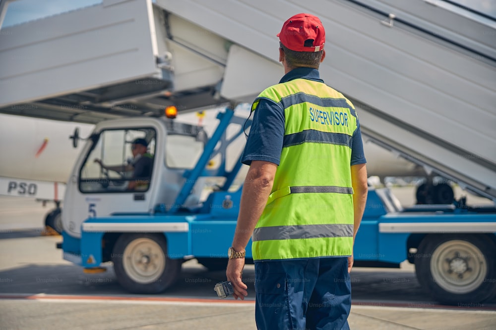 Vue arrière d’un employé de l’aéroport supervisant son collègue au volant d’un camion avec le passager montant dans les escaliers