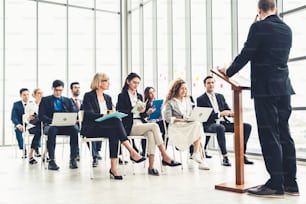 Group of business people meeting in a seminar conference . Audience listening to instructor in employee education training session . Office worker community summit forum with expert speaker .