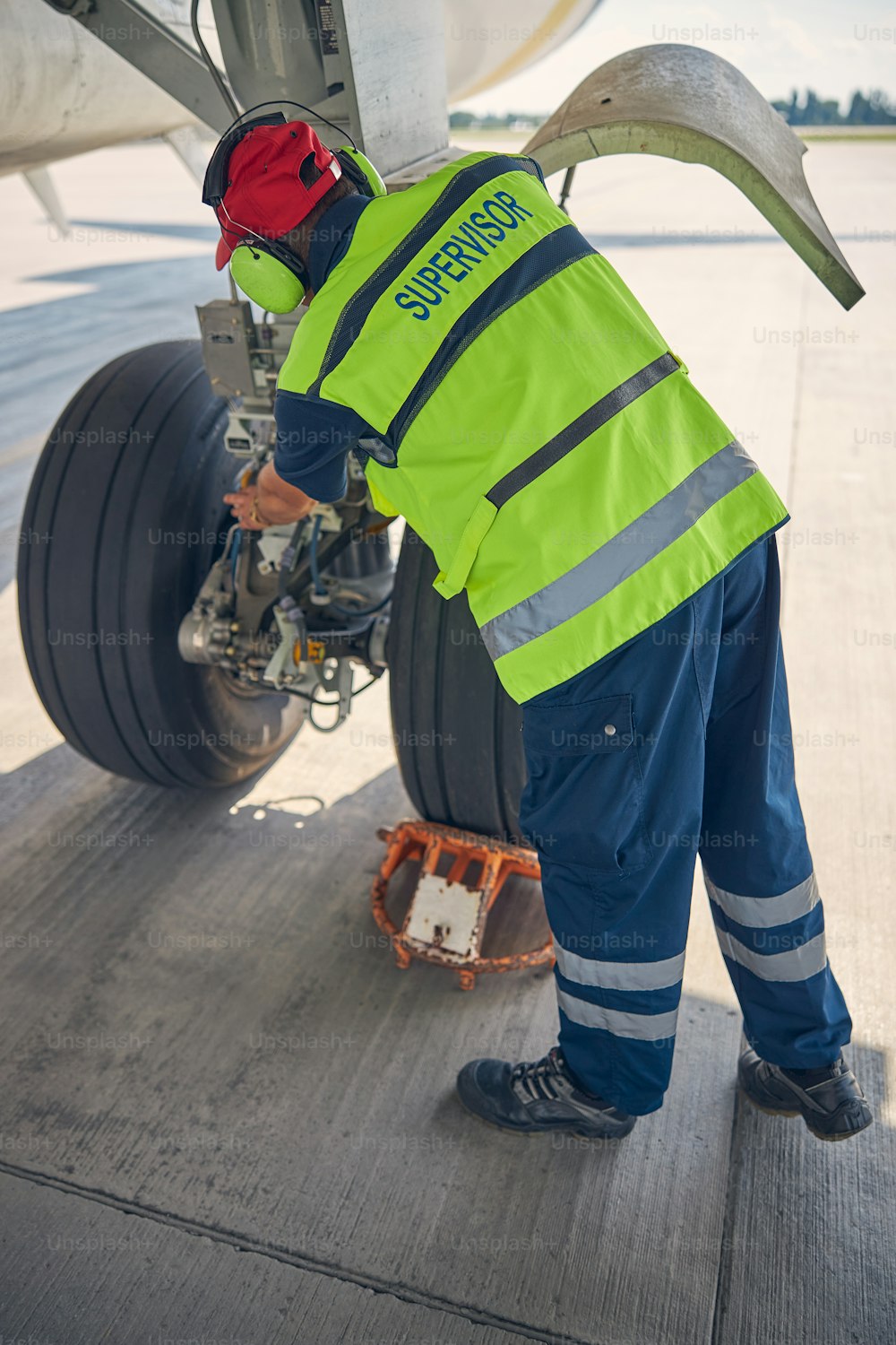 Back view of a qualified aircraft mechanic in a safety vest inspecting the plane wheels