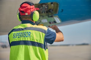 Vista trasera de un técnico realizando una inspección rutinaria de un avión de pasajeros en el aeródromo