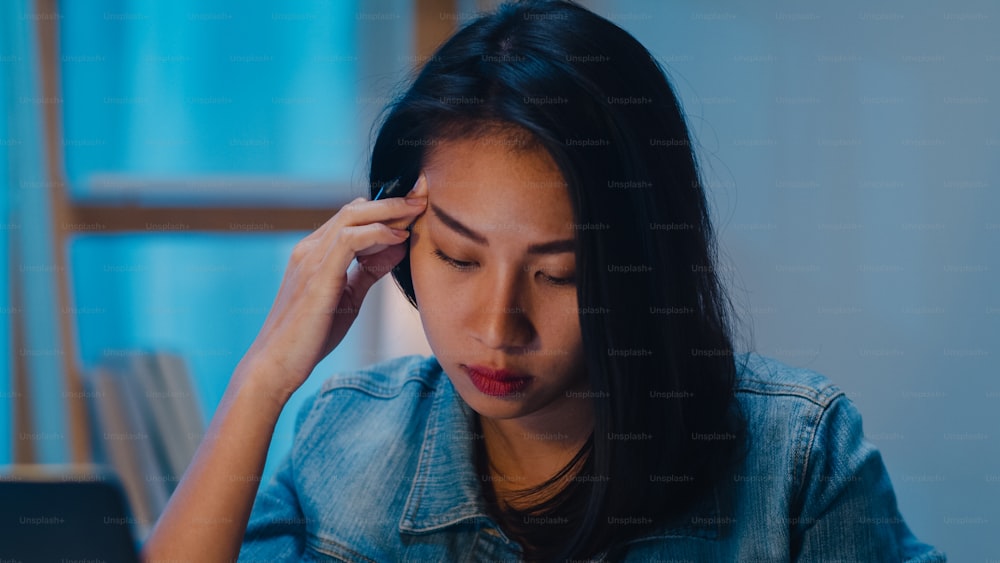늦은 밤에 일하는 밀레니엄 젊은 중국 사업가는 현대 가정의 거실에서 노트북으로 프로젝트 연구 문제로 스트레스를 받습니다. 아시아 사람들 직업적 소진 증후군 개념.