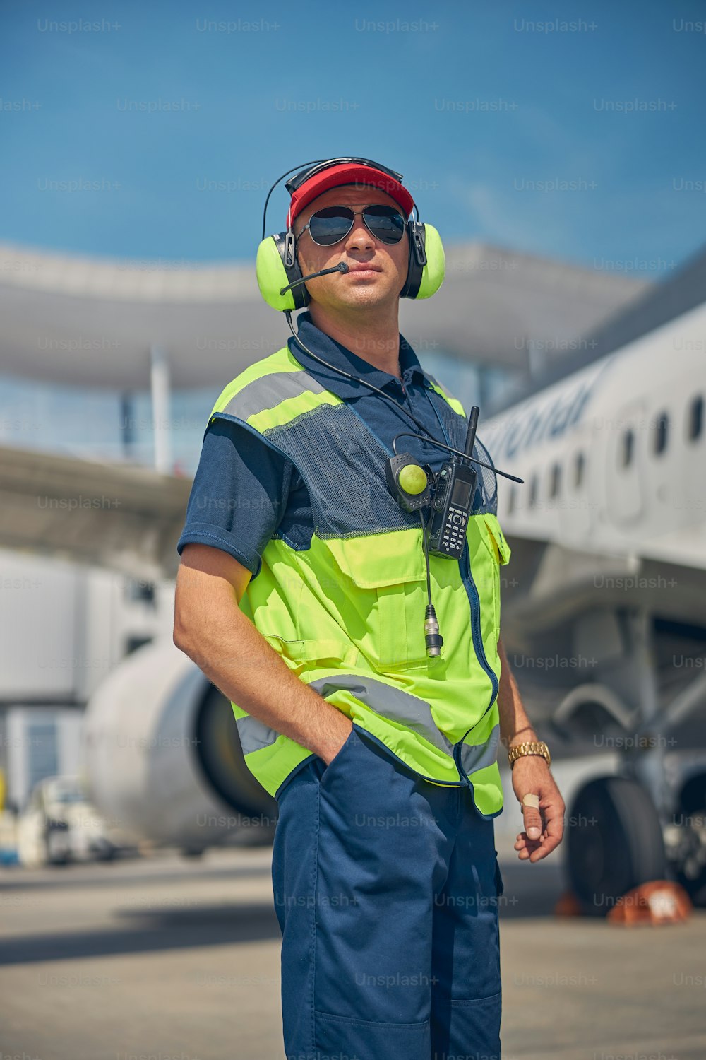 Front view of a serious Caucasian airport worker in noise-canceling headphones standing at an airdrome