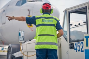 Back view of a man in noise-canceling headphones standing in front of a civil plane