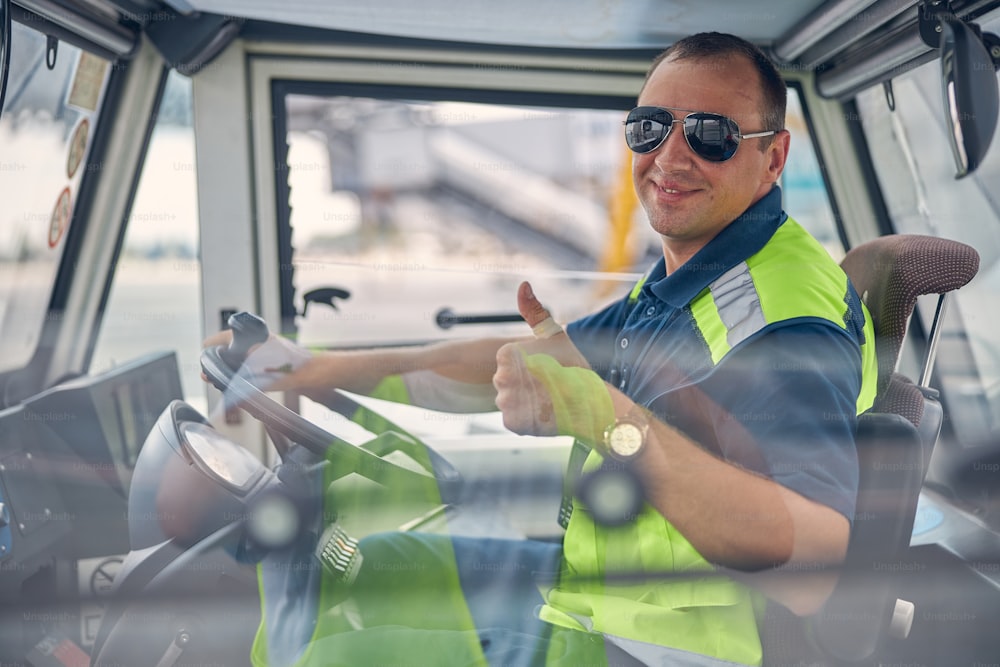 Front view of a pleased Caucasian truck driver in sunglasses showing a gesture of approval
