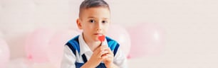 Happy Caucasian pensive child boy eating heart shape red lollipop. Valentine Day love holiday concept. Web banner header for website. Copyspace for text.