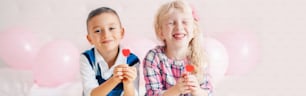 Happy Caucasian funny children eating heart shape red lollipops. Best friends forever. Valentine Day love holiday concept. Web banner header for website. Boy and girl laughing having fun.