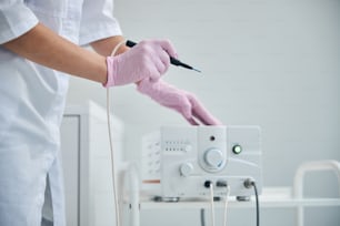 Cropped photo of a woman in latex gloves using the electrocautery machine for skin treatment