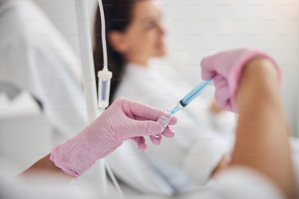 Qualified female nurse withdrawing a medication from an open glass ampule into a disposable syringe