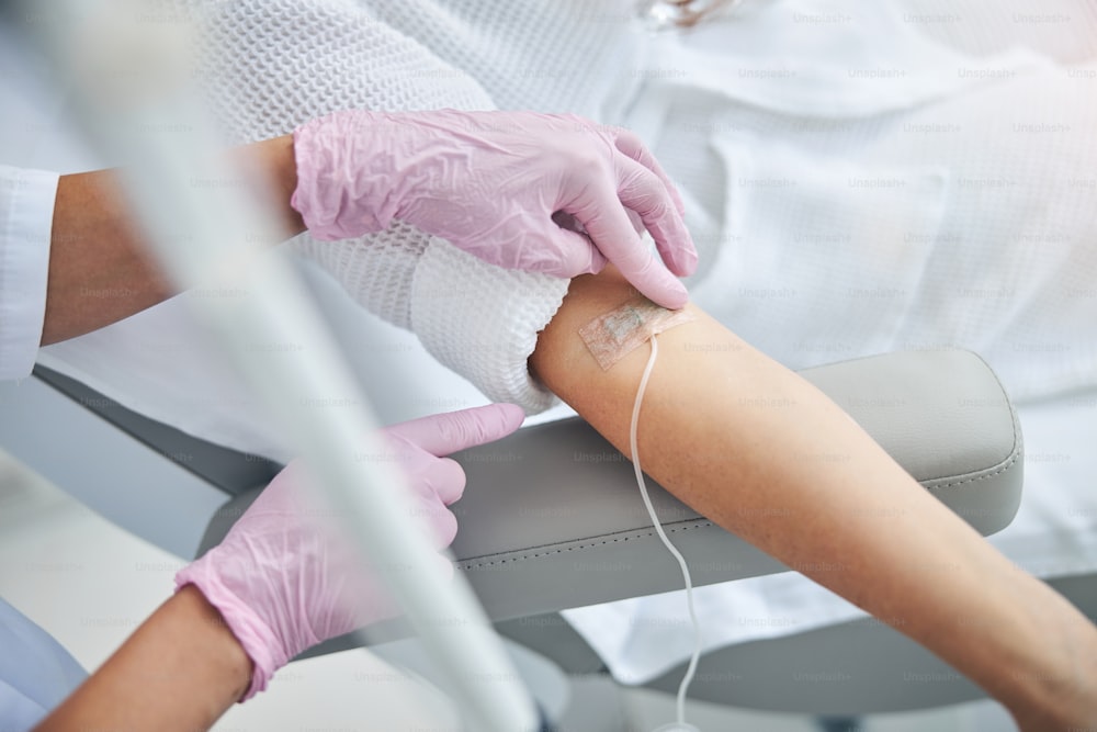 Cropped photo of a nurse in sterile gloves securing a catheter in a patient vein with an adhesive tape