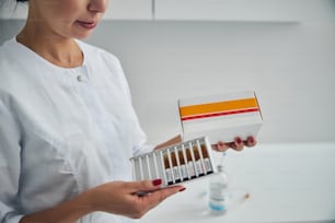 Cropped photo of a Caucasian doctor holding a carton box of ampules in her hands