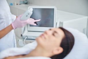 Dermatologue qualifiée ajustant les paramètres de traitement sur un échographe facial avant une intervention