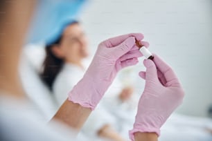 Cropped photo of a woman in disposable gloves holding a vitamin ampule in her hands
