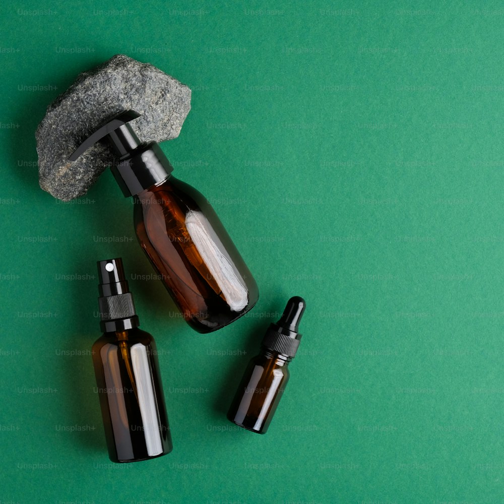 Amber glass cosmetic bottles and stone on green background. Flat lay, top view. Bio nature cosmetics skin care concept