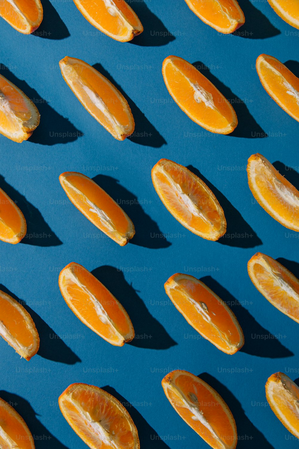 Creative pattern made with fresh orange slices against vibrant blue background. Minimal sunlit flat lay.