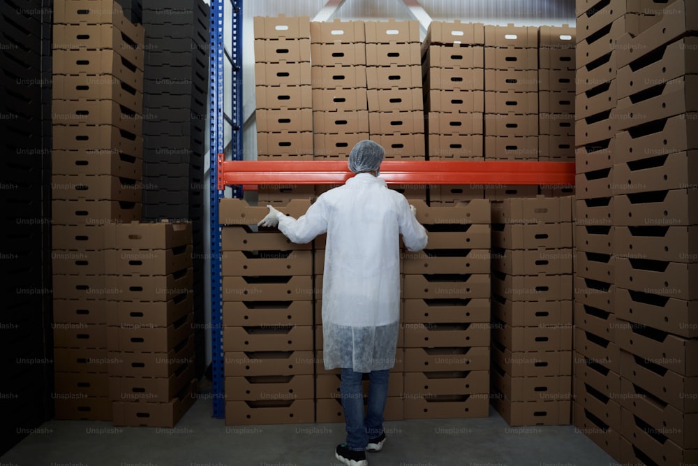 Back view of a man in a gauze cap and latex gloves arranging cardboard boxes