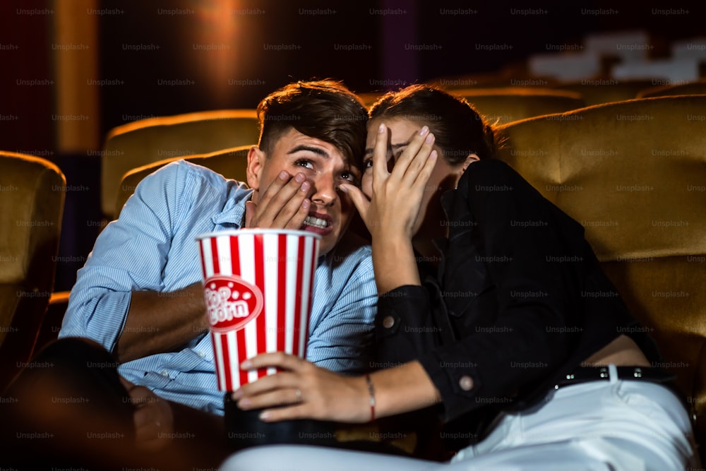 A couple of lovers watching movie shock and eyes close in the movie theater cinema.