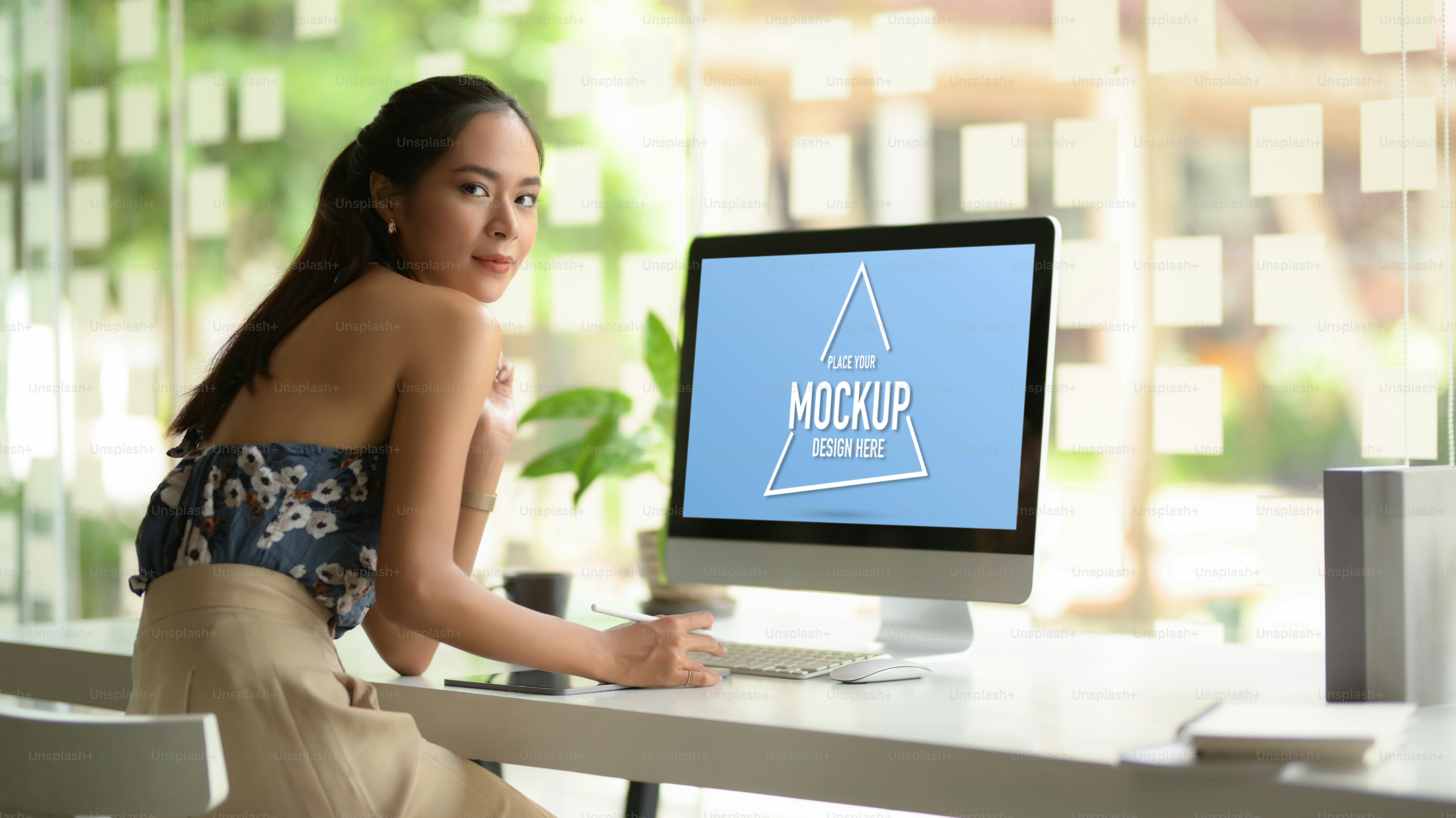 Portrait of female fashion designer looking into camera and smiling while working on computer table