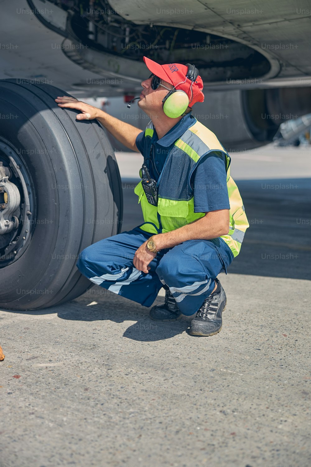 Side view of a focused Caucasian aircraft mechanic sitting on his haunches under the airplane