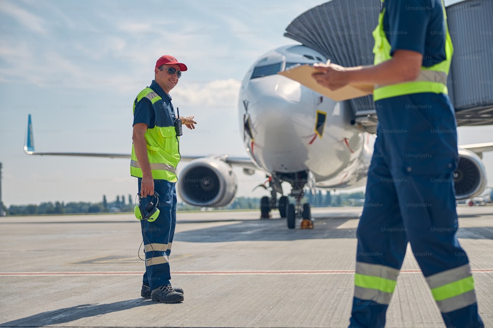 Ritratto a figura intera di un operaio maschio sorridente che indica un aereo al suo collega maschio