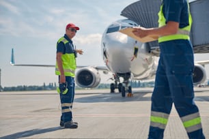 Retrato de cuerpo entero de un trabajador sonriente señalando un avión a su colega masculino