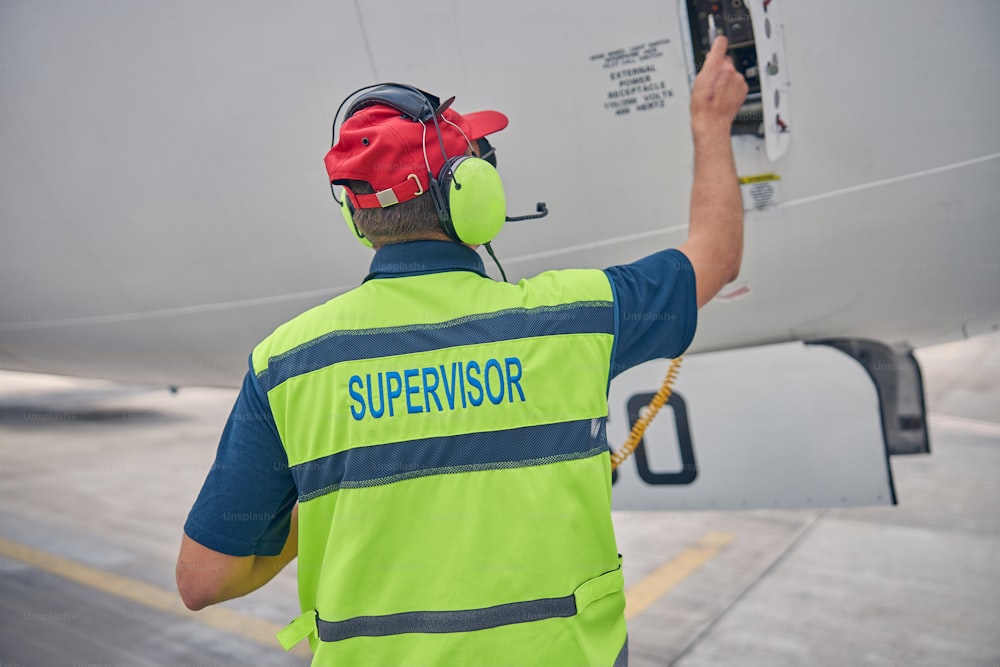 Vue arrière d’un technicien qualifié portant un casque d’écoute à l’aide d’un connecteur d’alimentation électrique externe d’avion