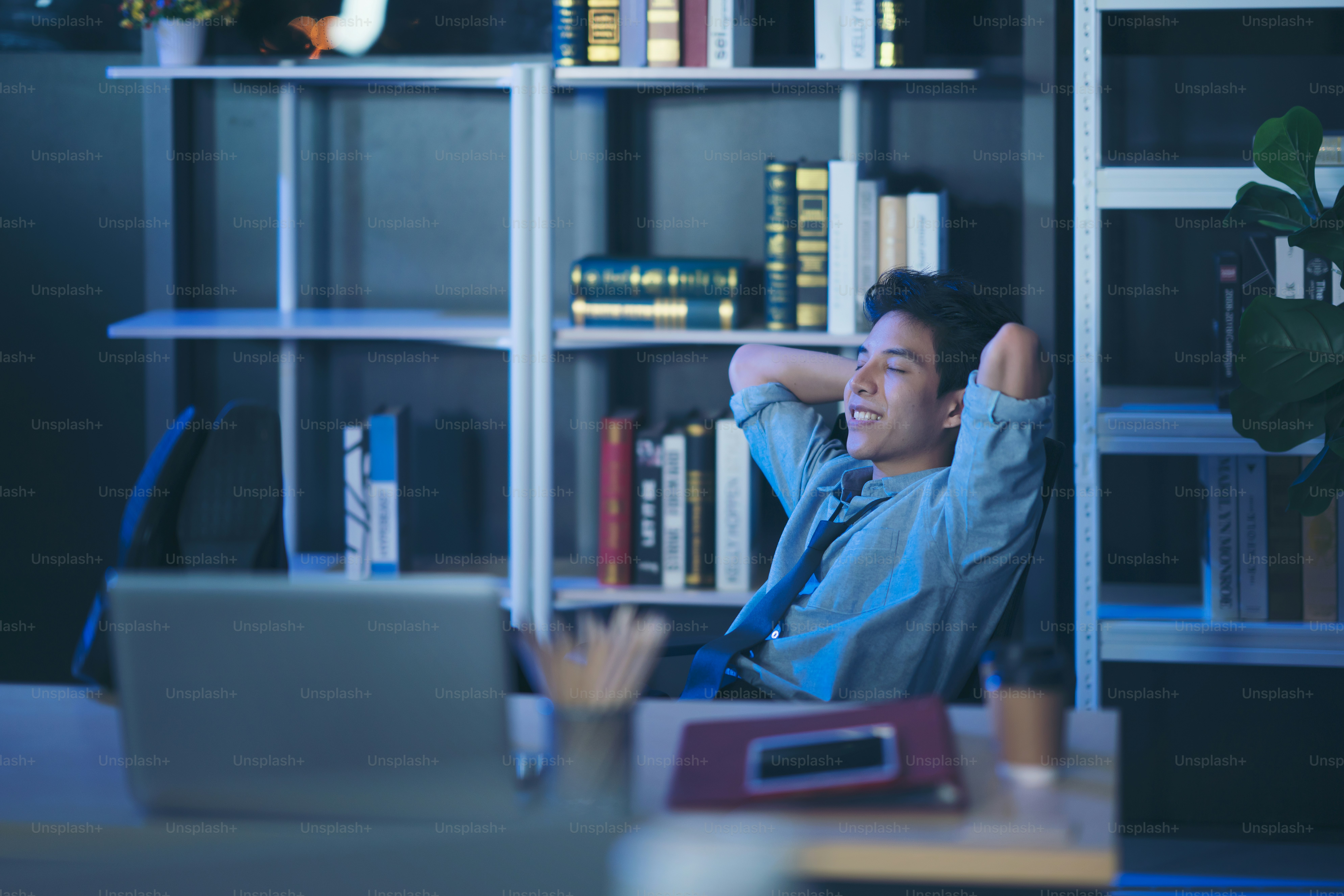 リラックスした自信のある若いビジネスマンは、オフィスで机の上に足を置いて寝る夜遅くに残業 テーブルフットレスト