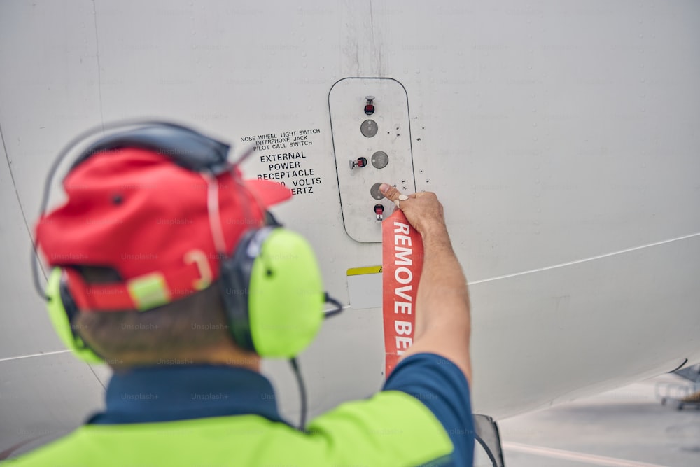 Back view of an experienced male aircraft maintenance engineer opening the external power access door