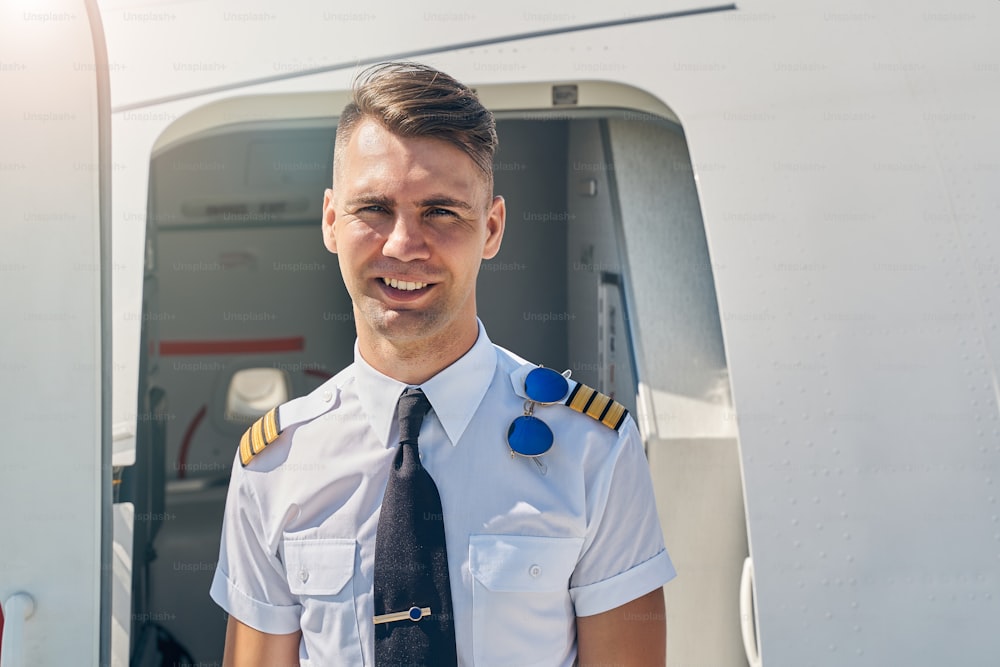 Close up portrait of a smiling airline male pilot standing in front of the aircraft entrance