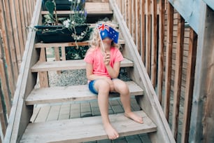 Adorable cute happy Caucasian girl holding Australian flag. Funny child kid covering her face with Australia flag. Little citizen celebrating Australia Day holiday in January outdoor.