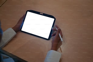 The top view of a woman is using a computer tablet with a white blank screen at the wooden table.