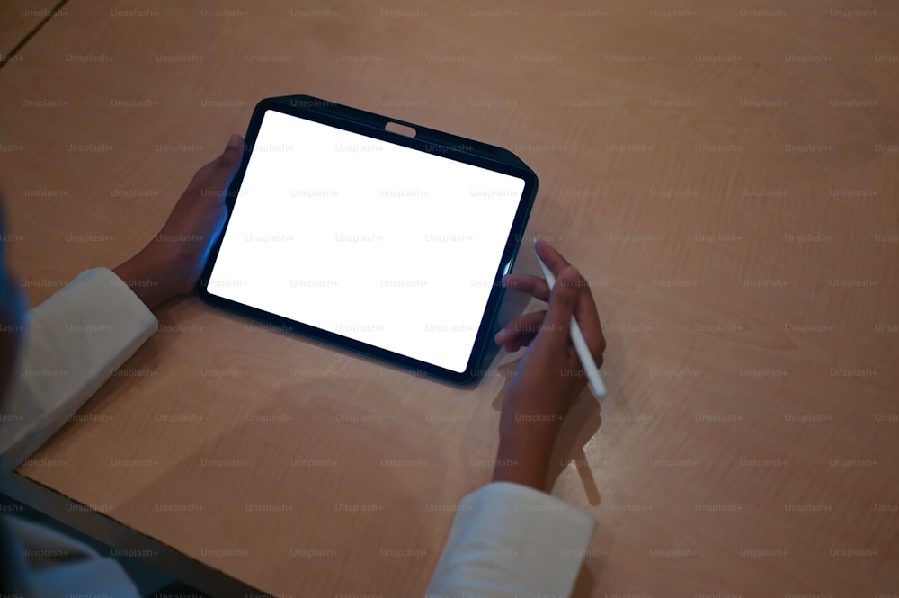 Die Draufsicht einer Frau ist ein Computer-Tablet mit einem weißen leeren Bildschirm am Holztisch.
