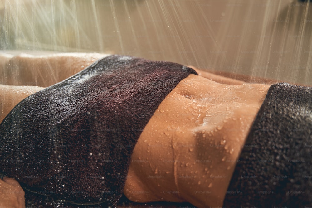 Ritratto ravvicinato di bella pancia di donna mentre ha pioggia di doccia per la salute
