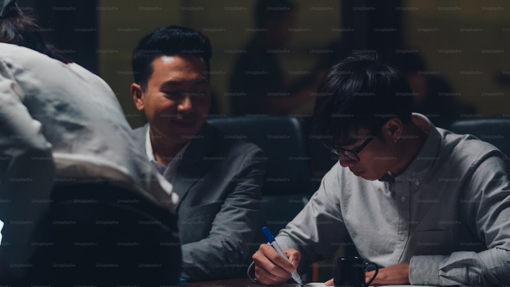 Uomini e donne d'affari dell'Asia millenaria che si incontrano, fanno brainstorming, idee su nuove scartoffie, colleghi di progetto, che lavorano insieme, pianificazione, strategia di successo, si godono il lavoro di squadra in un piccolo ufficio notturno moderno.