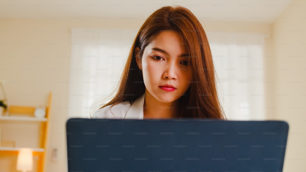 Retrato de ropa casual de mujeres asiáticas independientes usando una computadora portátil que trabaja en la sala de estar de casa. Trabajo desde casa, trabajo remoto, autoaislamiento, distanciamiento social, cuarentena para la prevención del coronavirus.
