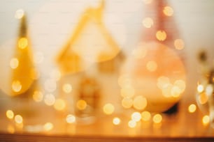 Abstract Christmas background. Yellow illumination bokeh on miniature fairy village. Blurred image of house and glitter trees in golden festive lights. Merry Christmas and Happy Holidays