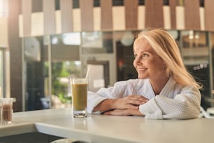 Waist up portrait of happy smiling woman in white soft bathrobe enjoying good place of spa resort hotel