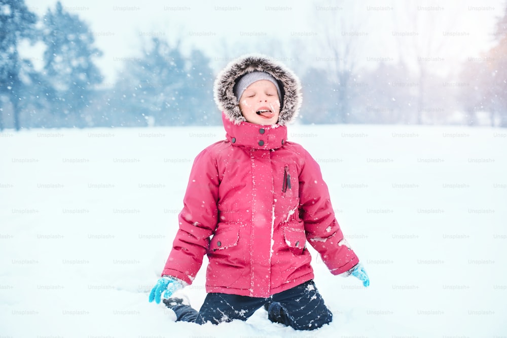 Cute adorable funny Caucasian excited girl child eating licking snow during cold winter snowy day. Kids outdoor seasonal activity. Happy candid authentic childhood lifestyle.