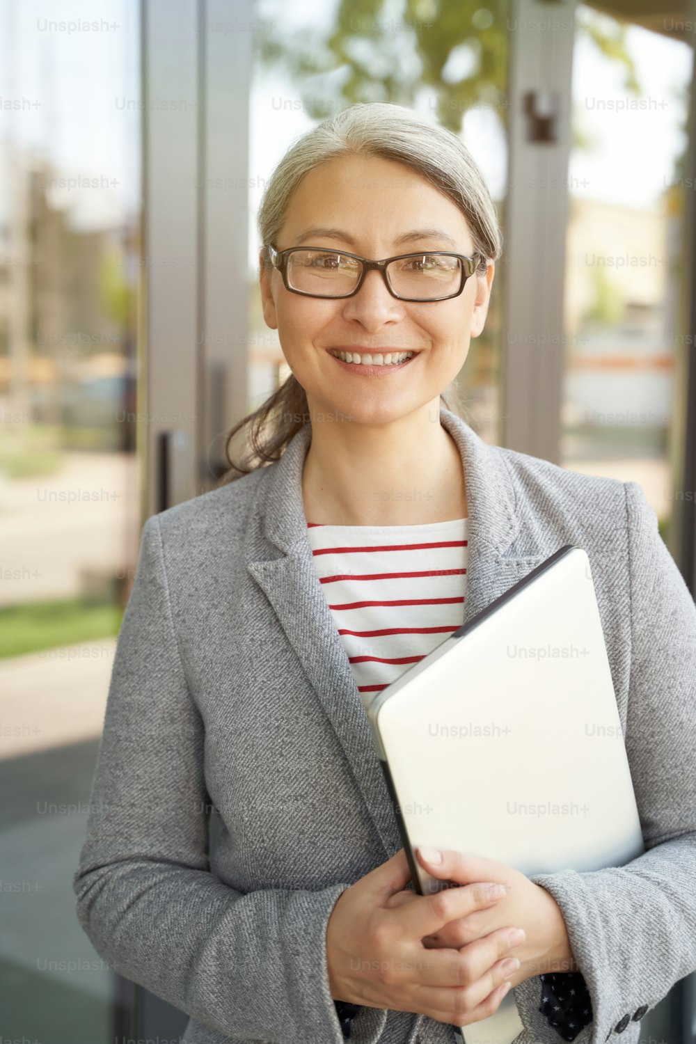 On the way to work. Vertical shot of a beautiful and happy senior lady, business woman holding laptop and smiling at camera while standing near office building. Business people, work concept