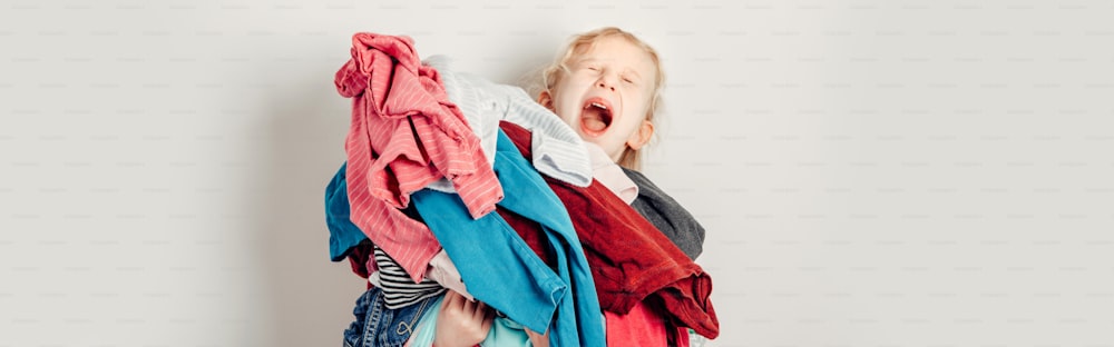 Mommy little helper. Adorable funny tired child arranging organazing clothing. Kid holding messy stack pile of clothes things. Home chores housework. Web banner header for website.