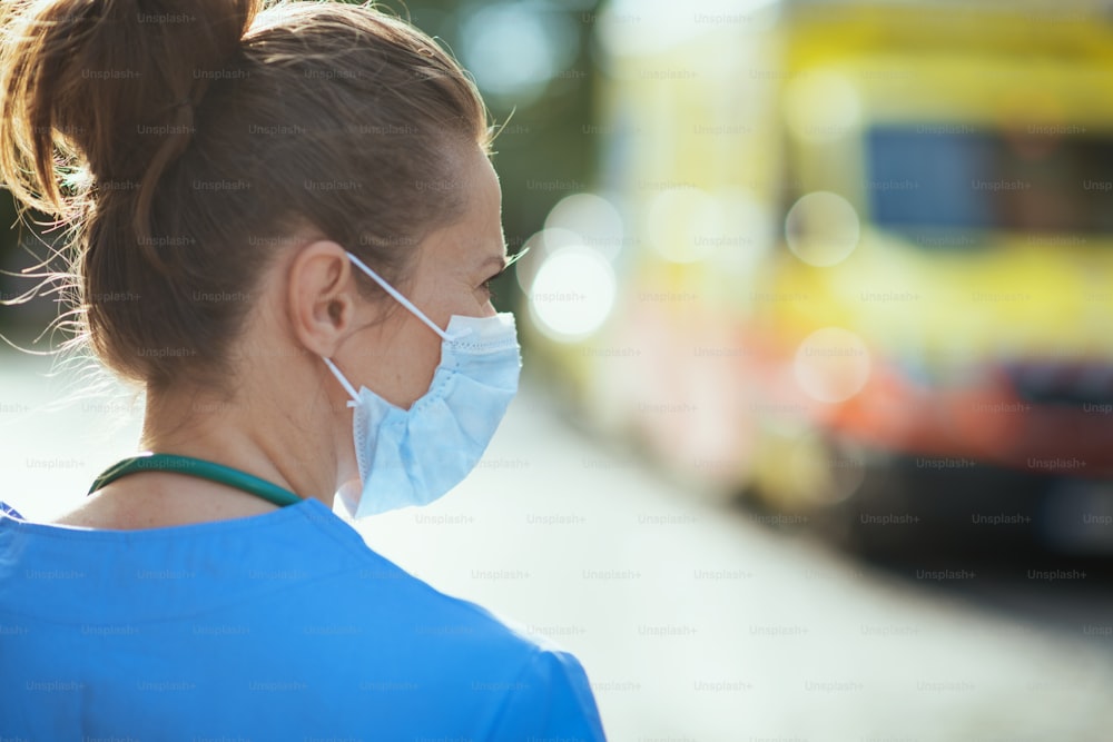 Pandemia di COVID-19. Visto da dietro la donna medico in uniforme con maschera medica all'esterno vicino all'ambulanza.