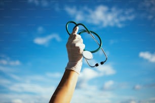 コロナウイルスパンデミック。聴診器とゴム手袋を空にぶつけた開業医の女性の接写。