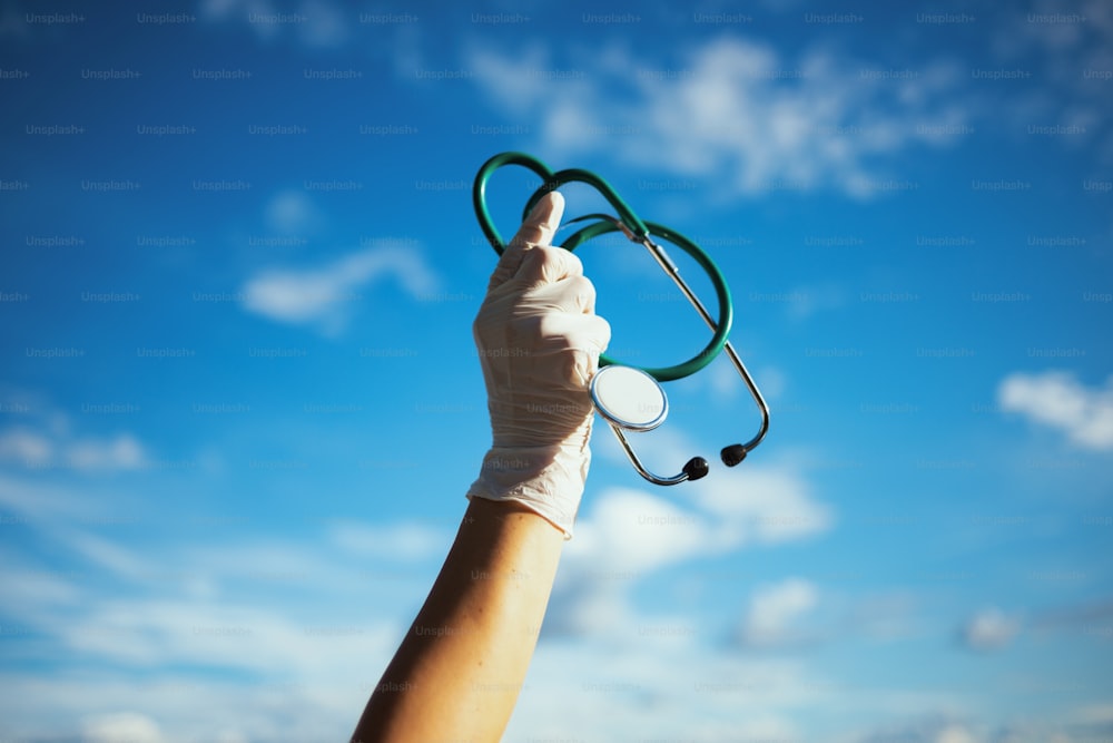 コロナウイルスパンデミック。聴診器とゴム手袋を空にぶつけた開業医の女性の接写。