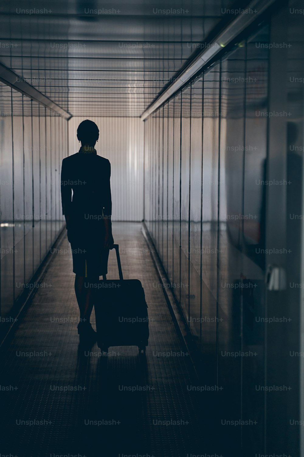 Back view of a slender woman in uniform standing with her baggage in the corridor
