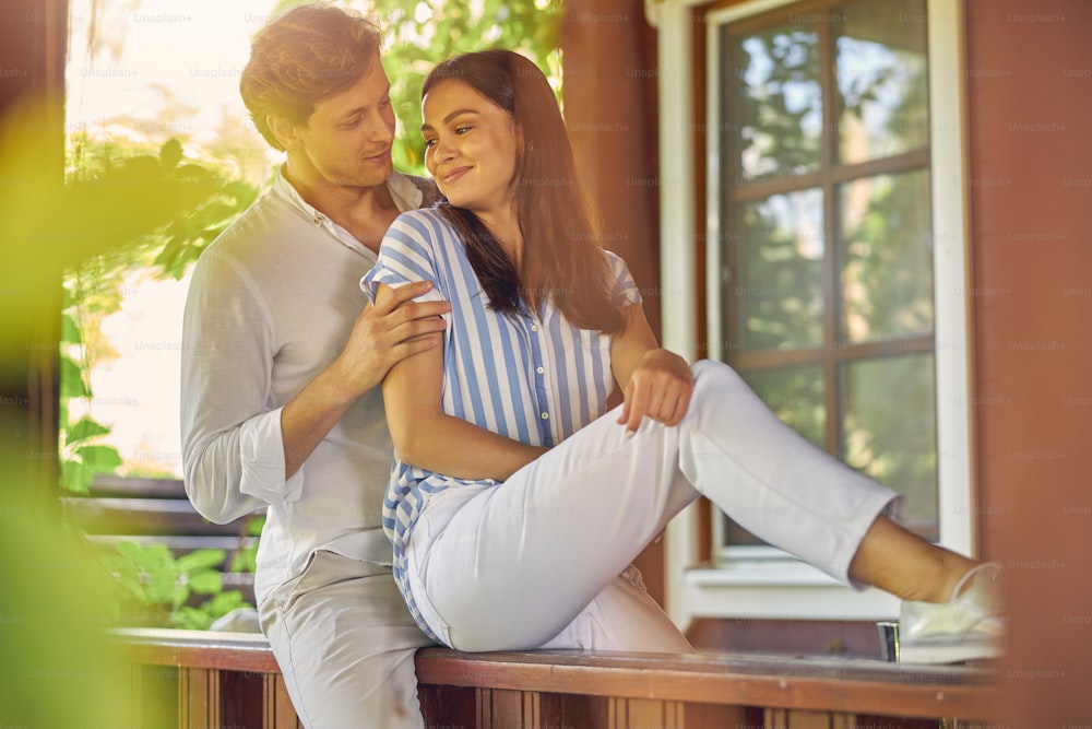 Close up portrait of beautiful couple wearing white clothing while resting in the outdoors in front of their house
