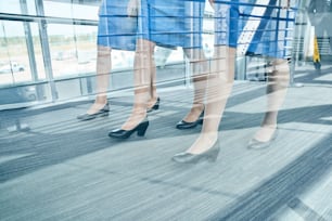 Cropped photo of three pairs of slender legs in leather court shoes walking along the airport terminal